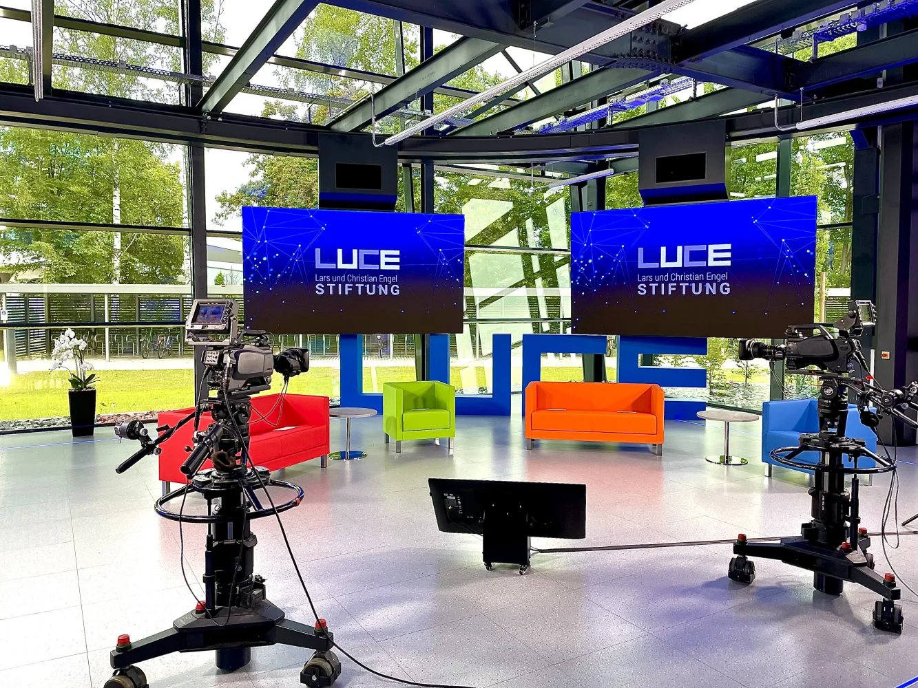 Streaming-Studio mit Studiokameras, Sofas und zwei Displays